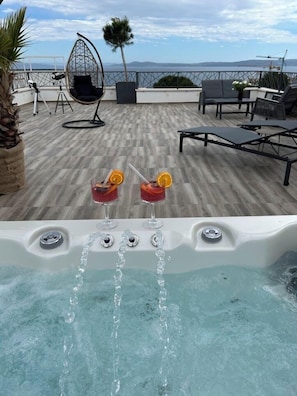 Una terraza en la azotea con jacuzzi, sillones de descanso y vista al mar.