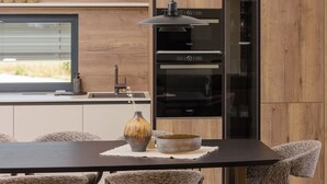 A modern kitchen with a dark countertop, a vase, and a bowl on a placemat. - Apartment Azure Pine (Okrug)