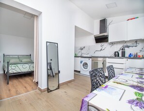 A compact living space with a bed, a washing machine, a dining table, and a kitchen area. - Apartment Panorama Nicolas (Kastela)