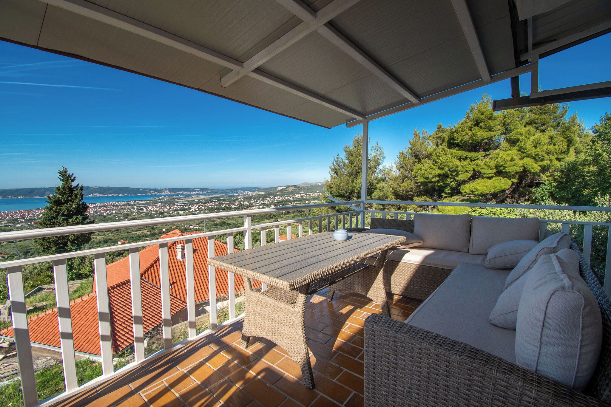 Une terrasse extérieure couverte, dotée d’une table et de sièges, offrant une vue panoramique sur une ville et la côte.