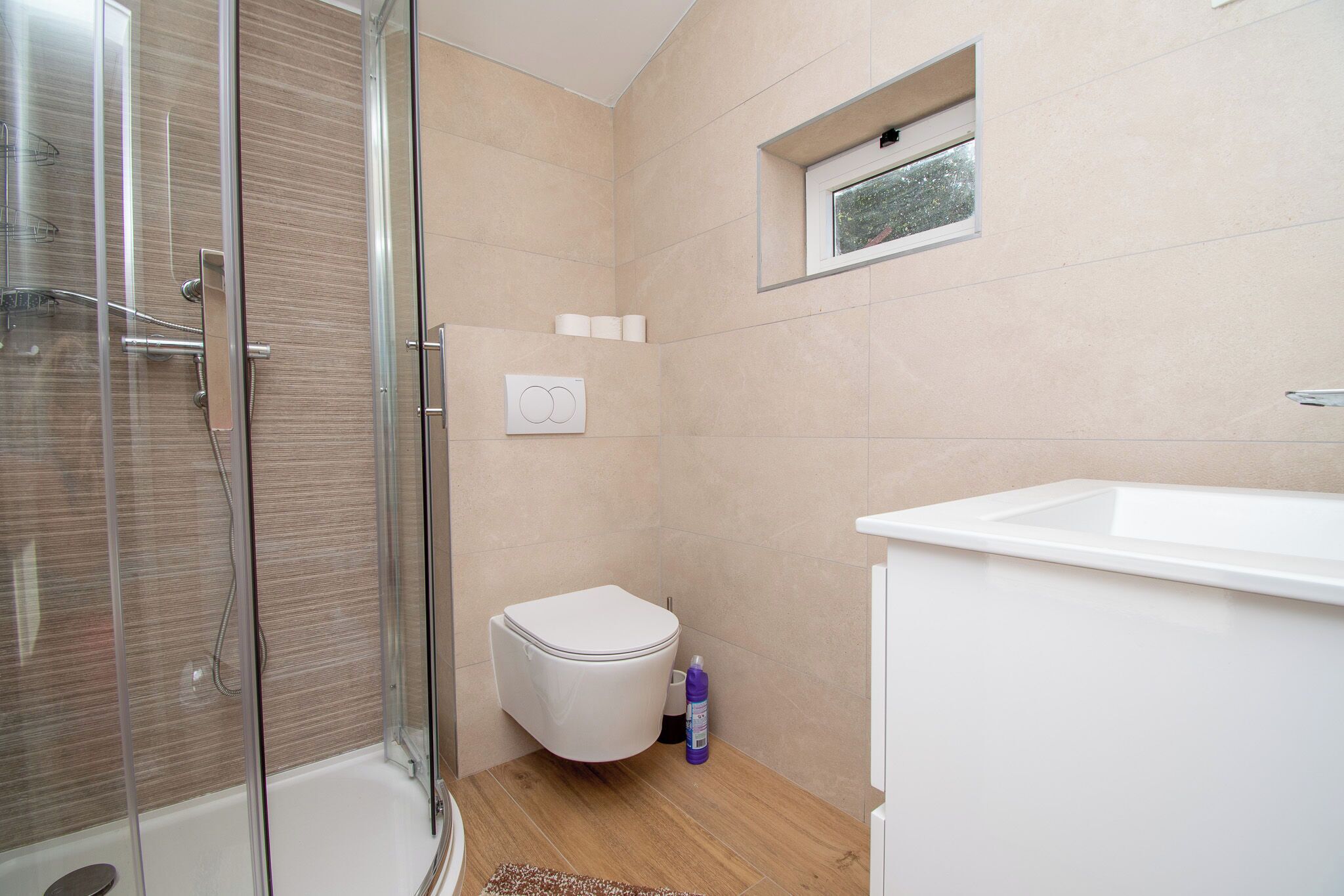 A bathroom with a glass shower enclosure, a toilet, a sink, and a small window.