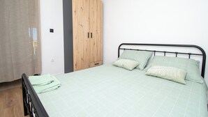 A bedroom with a bed, a wooden wardrobe, and a window with a sheer curtain. - Apartment Panorama Nicolas (Kastela)