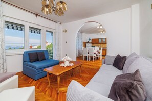 A living room with a sofa, a dining table, and a kitchen in the background. - Apartment Antonija (Novi Vinodolski)