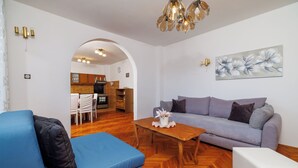 Een woonkamer met een bank, een bijzettafeltje en een eethoek met stoelen en een tafel.