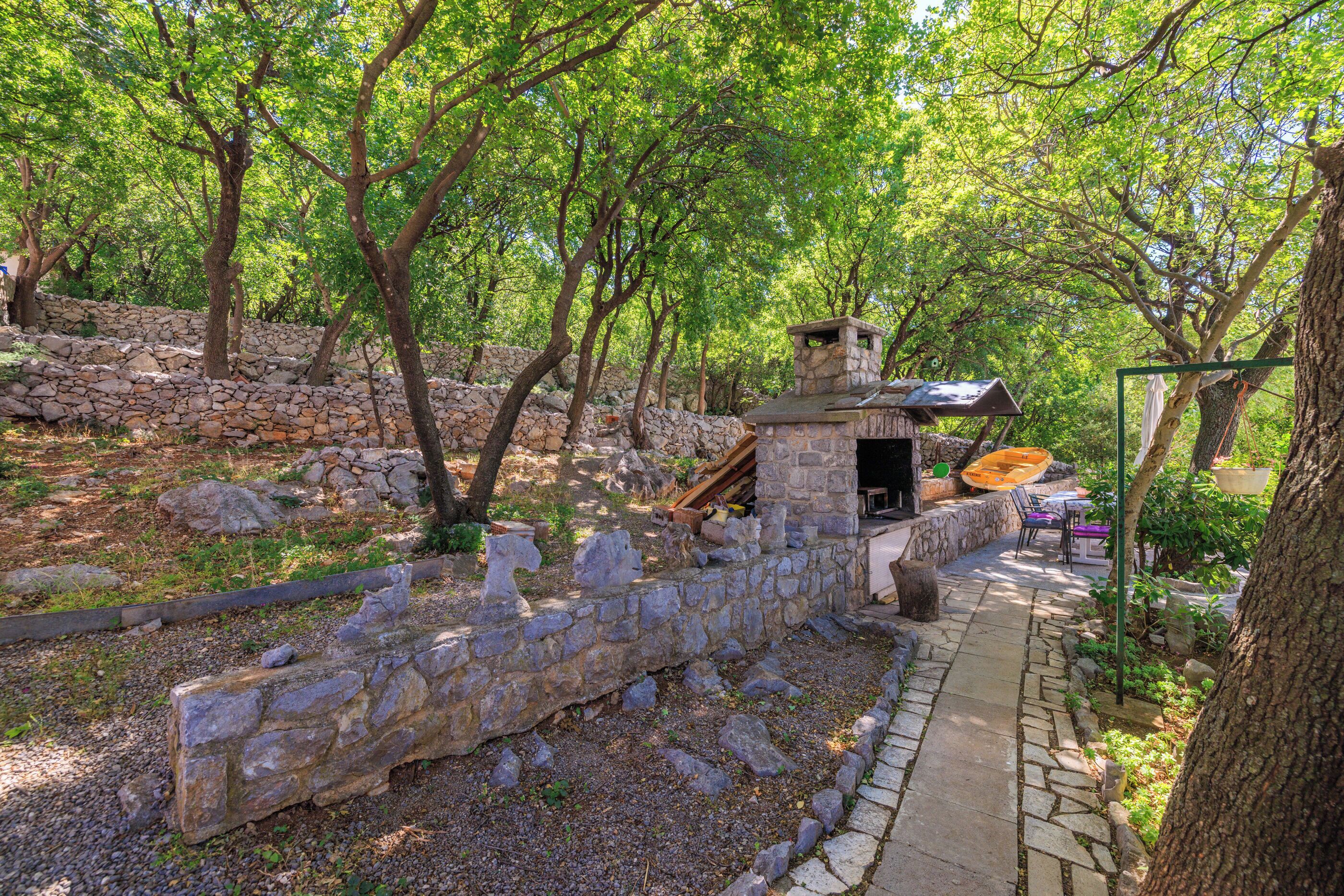 A stone pathway leading to a stone structure with a roof, surrounded by trees and greenery.