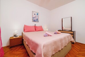 A bedroom with a bed, a nightstand with a lamp, a mirror, and a wall-mounted picture. - Apartment Antonija (Novi Vinodolski)