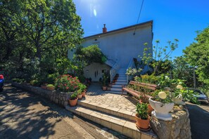 A house with a stone staircase leading to a door, surrounded by potted plants and a clear blue sky. - Apartment Antonija (Novi Vinodolski)