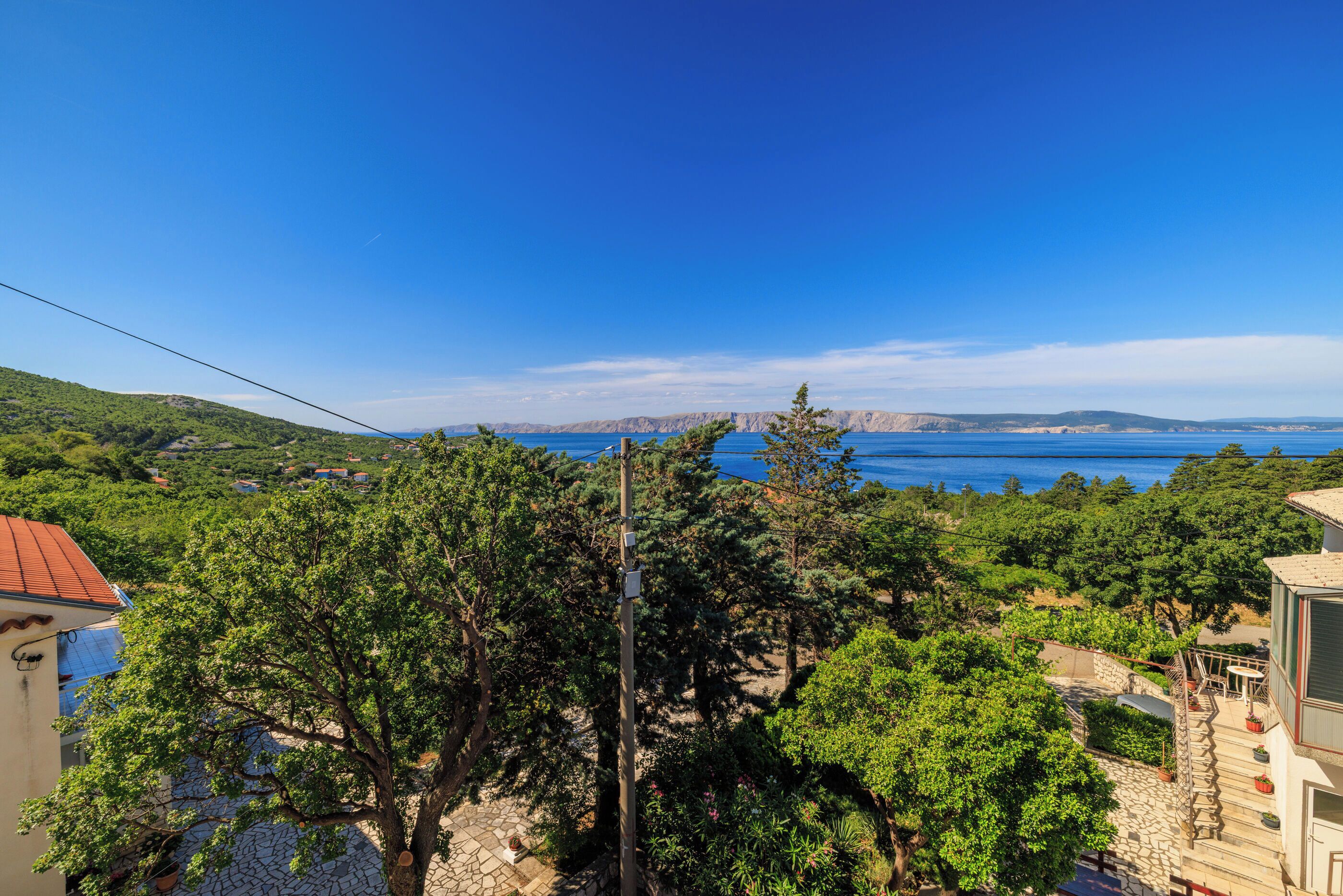 A coastal view with a clear sky, a stone pathway, and a building with a red roof.