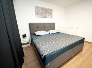 A bedroom with a bed, a nightstand, a wall-mounted picture, and a radiator. - Apartment Hope (Zmijavci)