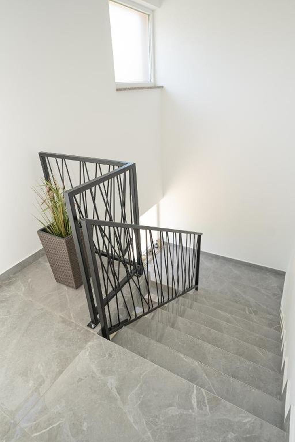 Een trap met een metalen leuning, een potplant en een raam.