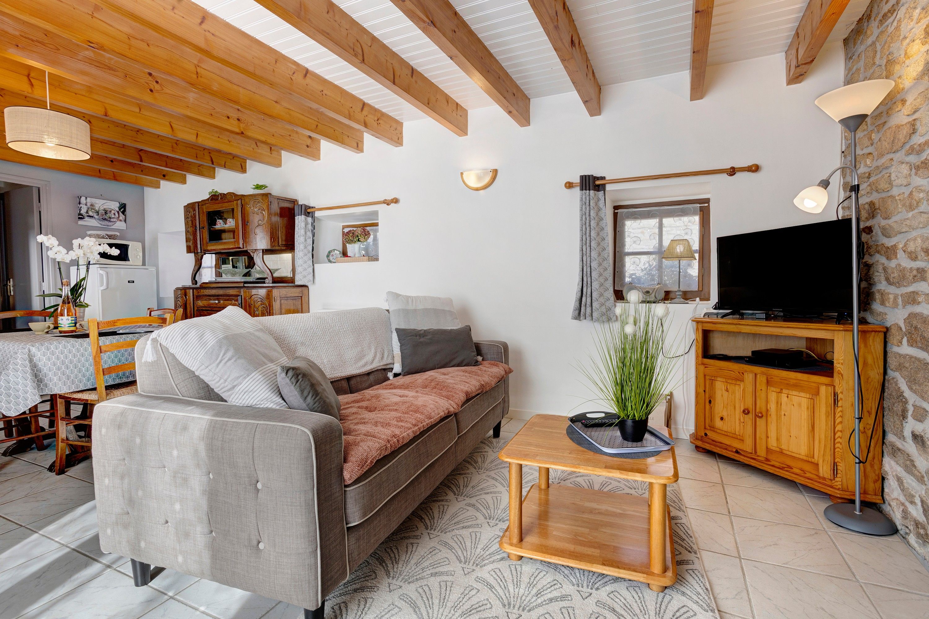 Un salon comprenant un canapé, un téléviseur, un meuble en bois et un coin repas avec une table et des chaises.
