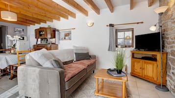 Ein Wohnzimmer mit einer Couch, einem Fernseher, einem Holzkabinett und einem Essbereich mit Tisch und Stühlen.