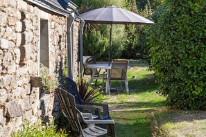 An outdoor seating area with a table and chairs, a large umbrella, and a stone wall.