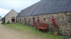 A stone building with a sloped roof, a bench, and potted plants.