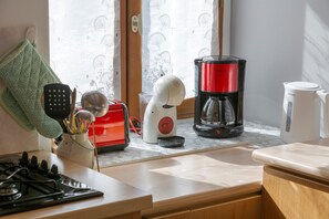 Una cocina con estufa a gas, una cafetera roja, un hervidor eléctrico blanco y un guante de cocina verde sobre la encimera.
