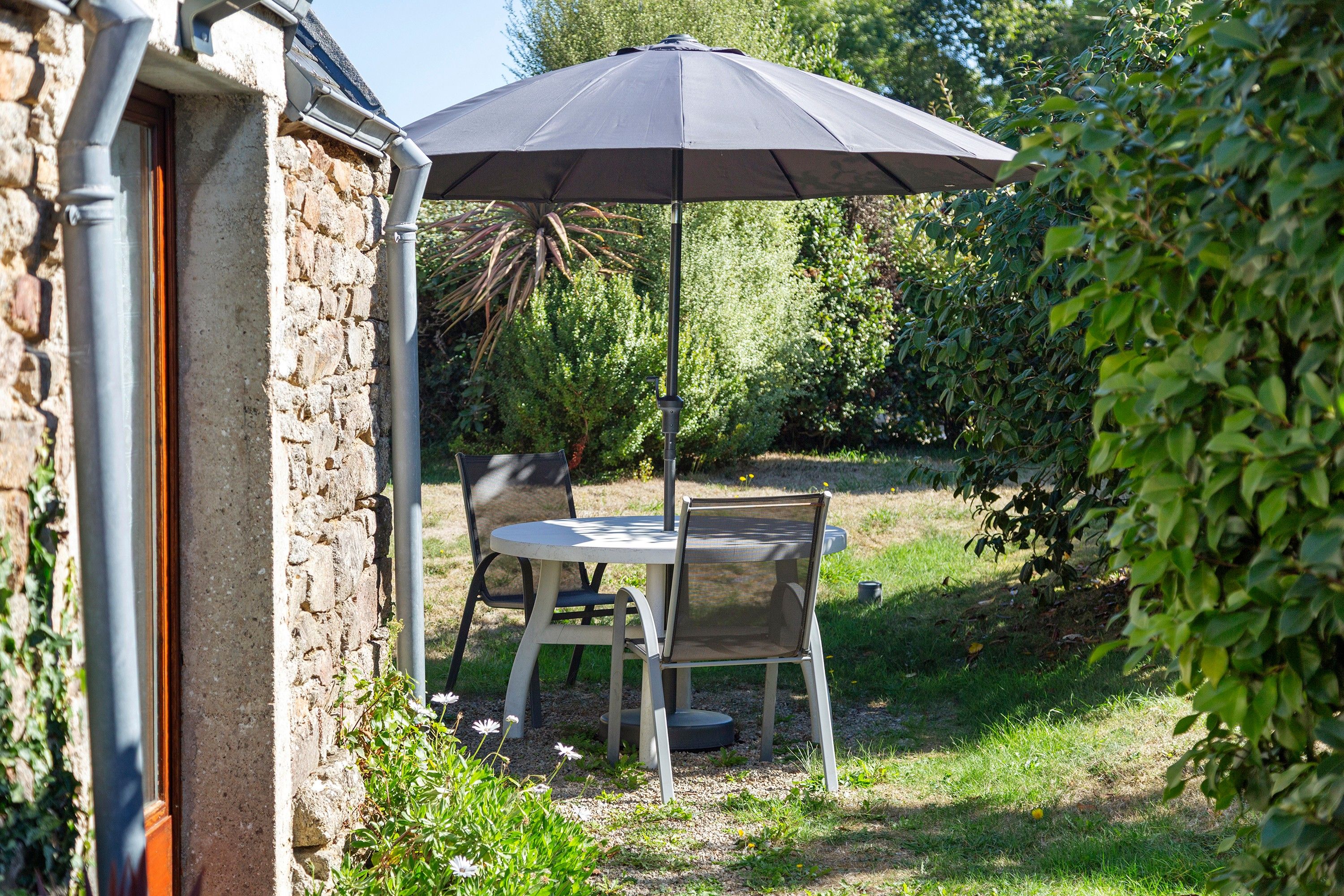 An outdoor patio with a table and chairs, a black umbrella, and a stone wall.