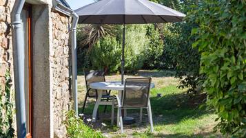 An outdoor patio with a table and chairs, a black umbrella, and a stone wall.