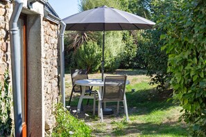 Une terrasse extérieure avec une table et des chaises, un parasol noir et un mur en pierre.