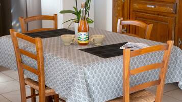 A dining table with a geometric patterned tablecloth, two wooden chairs, a bottle of Cidre extra-brut, two cups, and a plant.