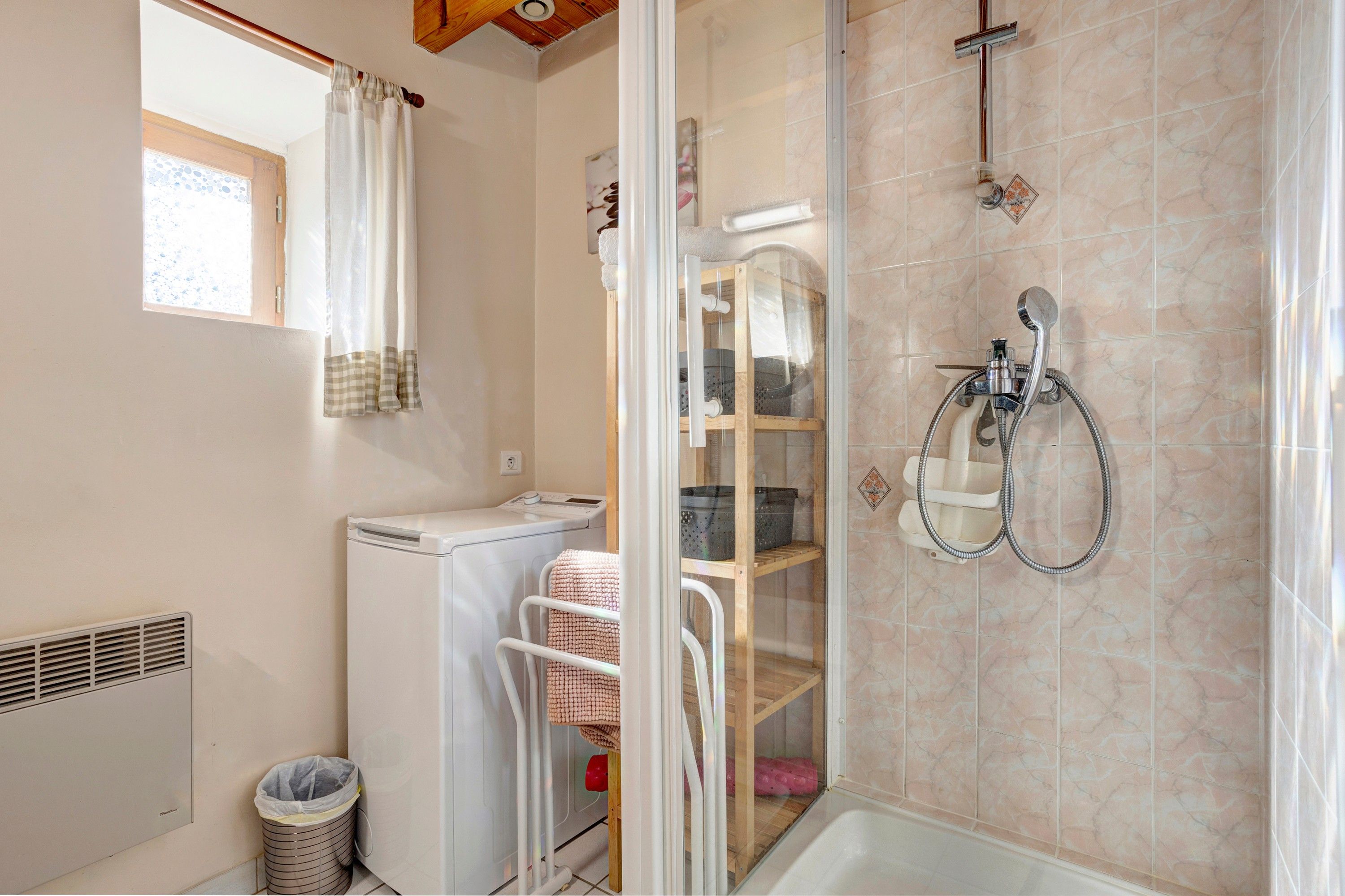 A bathroom with a shower, a drying rack, a washing machine, and a waste bin.
