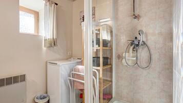 A bathroom with a shower, a drying rack, a washing machine, and a waste bin.