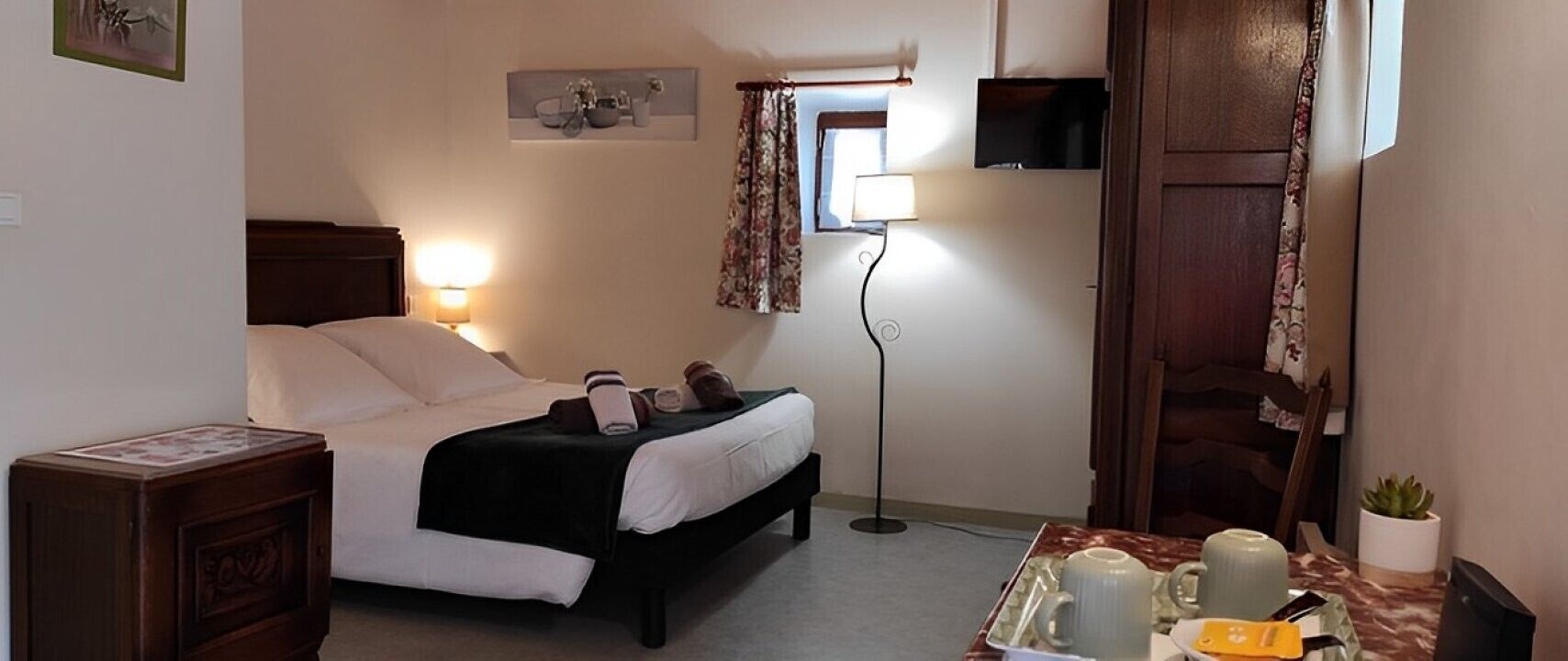 A bedroom with a bed, bedside table, lamp, and a small table with a kettle and cups.
