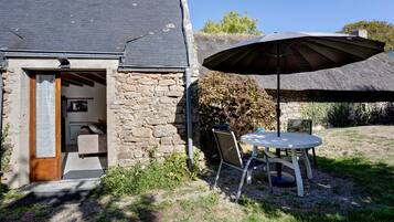 Un bâtiment en pierre avec un toit de chaume, une porte en bois et un petit patio comprenant une table et des chaises.