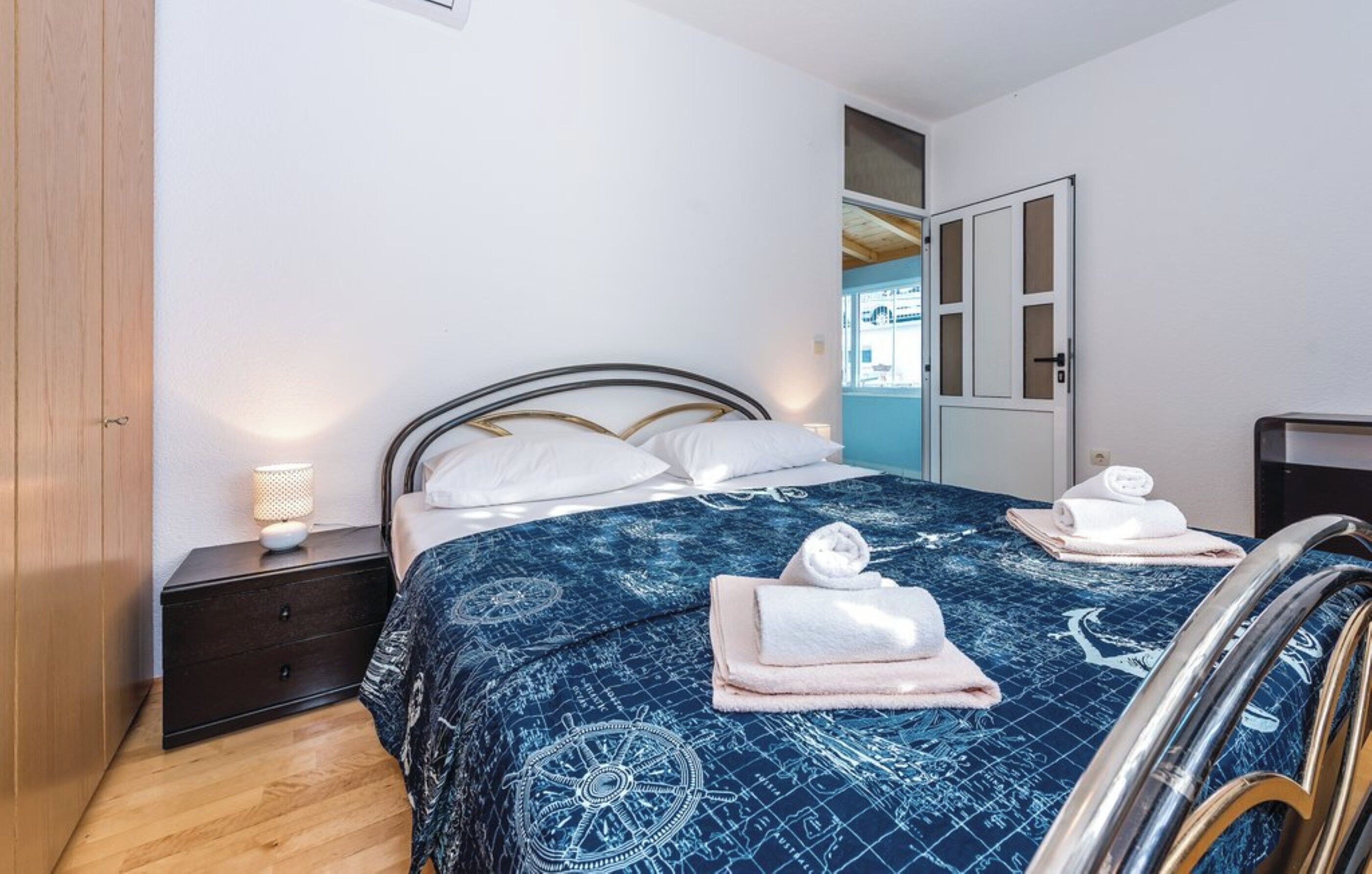 A bedroom with a bed, a nightstand, a lamp, and a door leading to another room.