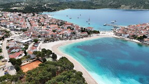 An aerial view of a coastal town with a beach, clear blue waters, and boats. - House Veronika (Primosten)