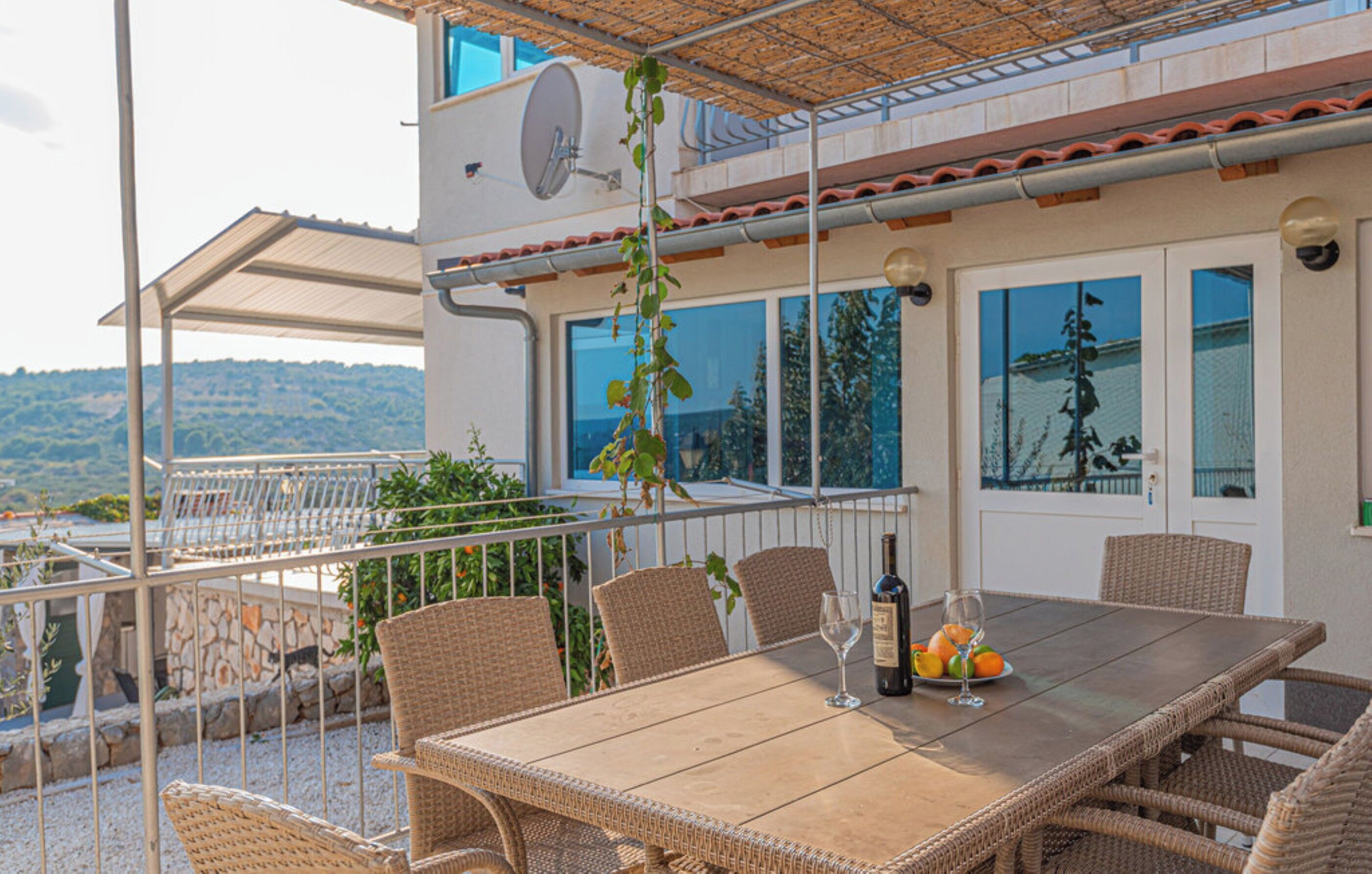 An outdoor dining area with wicker chairs and a table, a bottle of wine, and a glass.