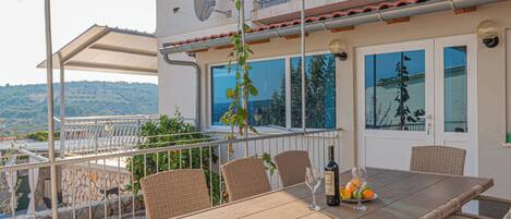 An outdoor dining area with wicker chairs and a table, a bottle of wine, and a glass.