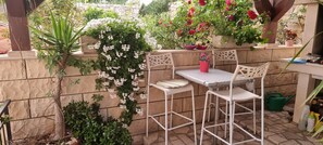 Eine Terrasse mit Tisch und Stühlen, umgeben von Kübelpflanzen und einer Steinmauer.
