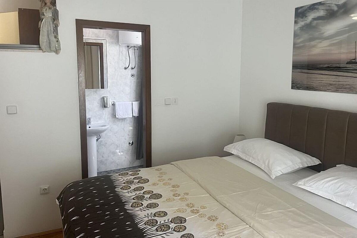 A bedroom with a bed, a nightstand, a painting, and a bathroom door.