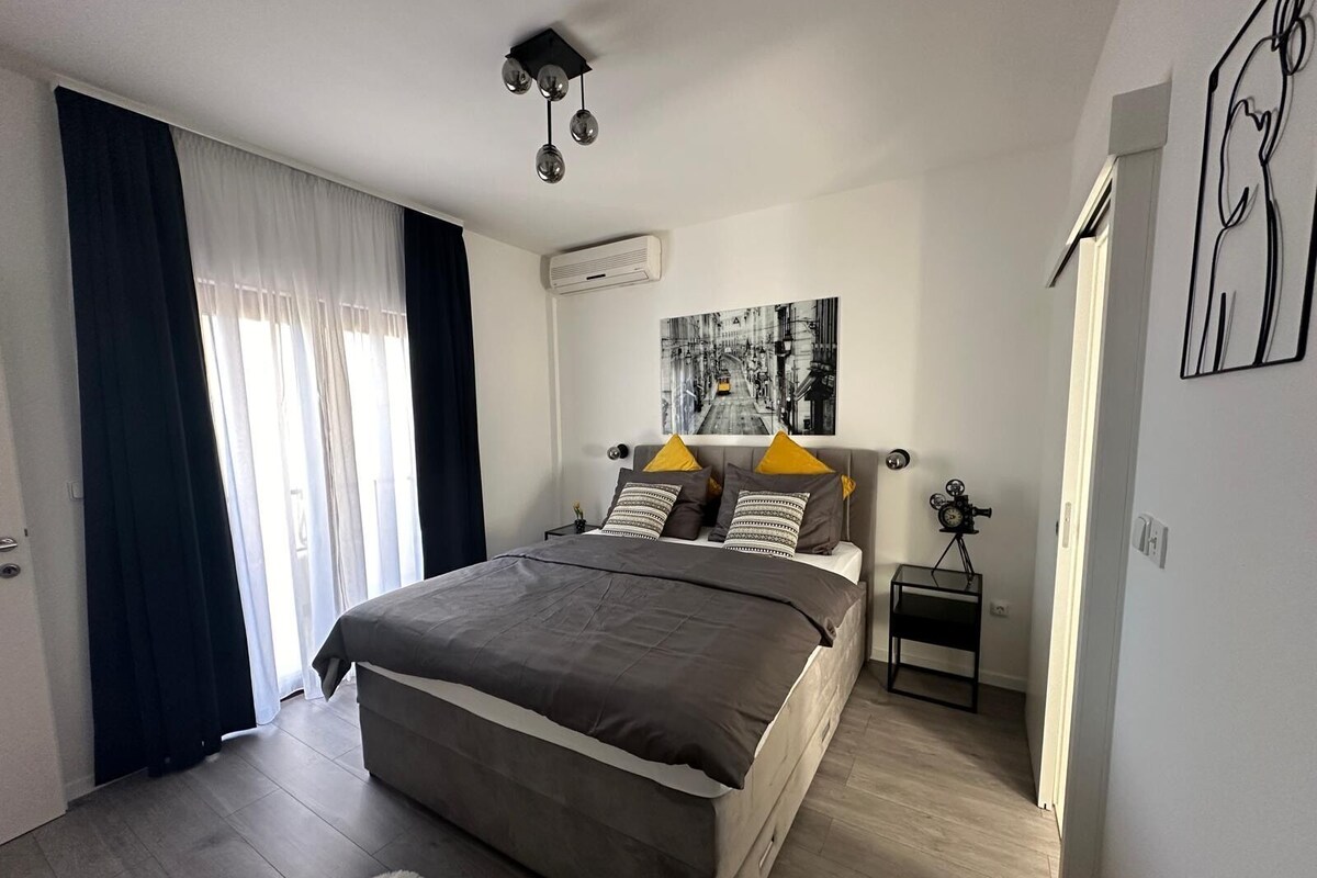 A modern bedroom with a bed, a bedside table, a wall-mounted air conditioner, and a window with curtains.