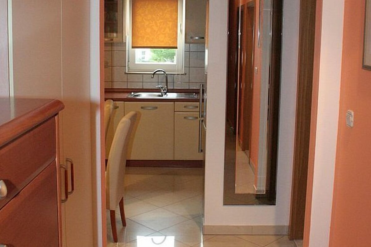 A narrow hallway leading to a kitchen with a window, a sink, and cabinets.