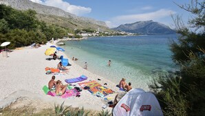 A beach with clear water, people sunbathing, and a mountain in the background. - Apartments Vila Paula (Dugi Rat)