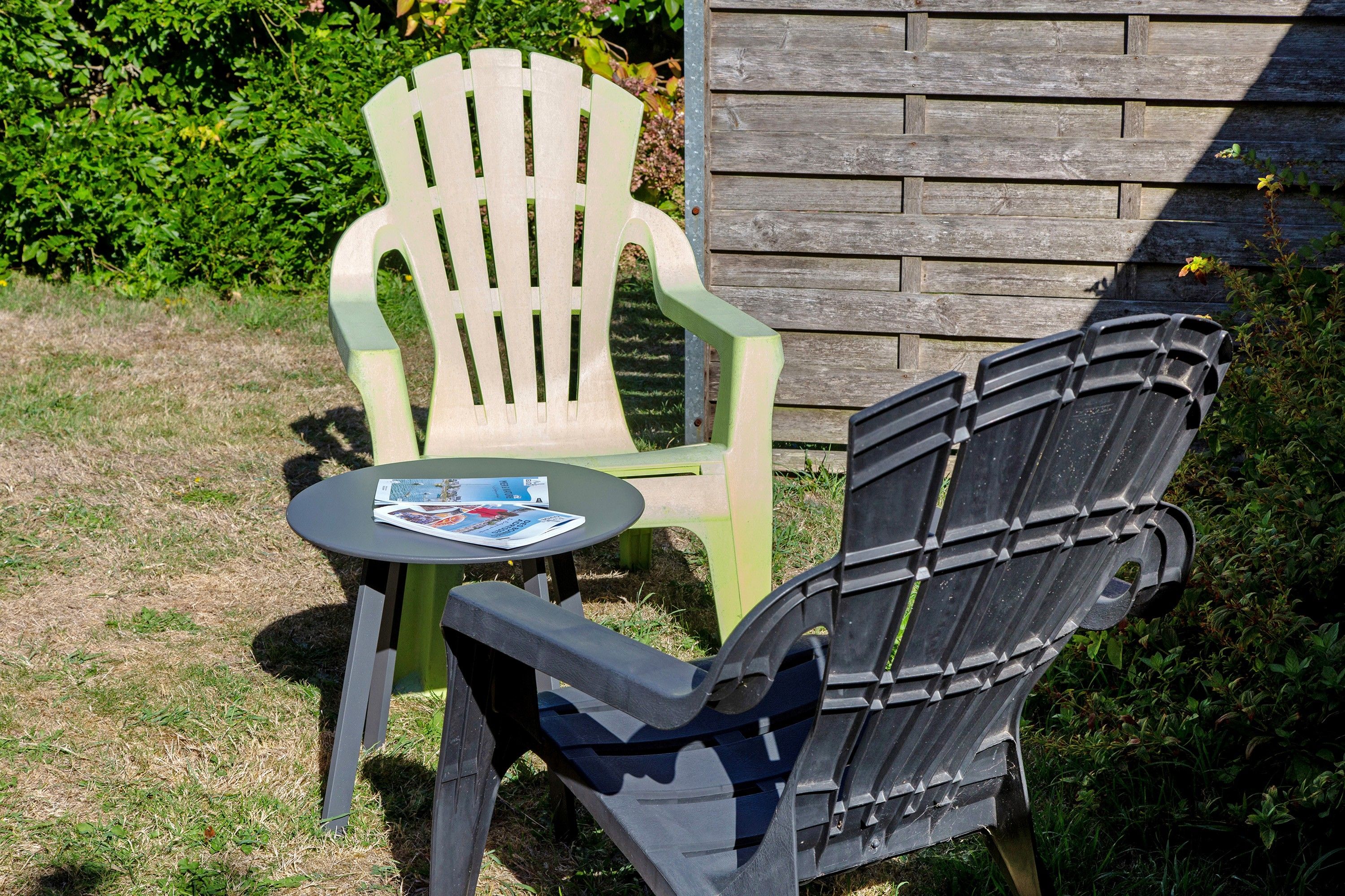 Deux fauteuils Adirondack, l’un vert et l’autre noir, avec une petite table ronde et un magazine posé entre eux.