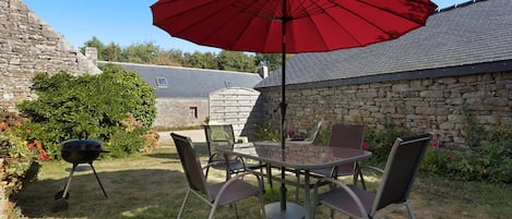 Un patio exterior con mesa y sillas, un paraguas rojo y una parrilla.