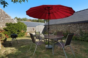 An outdoor patio with a table and chairs, a red umbrella, and a barbecue grill. - Holiday home 'Maison de vacances' 10min from beaches and GR34 (Mahalon)