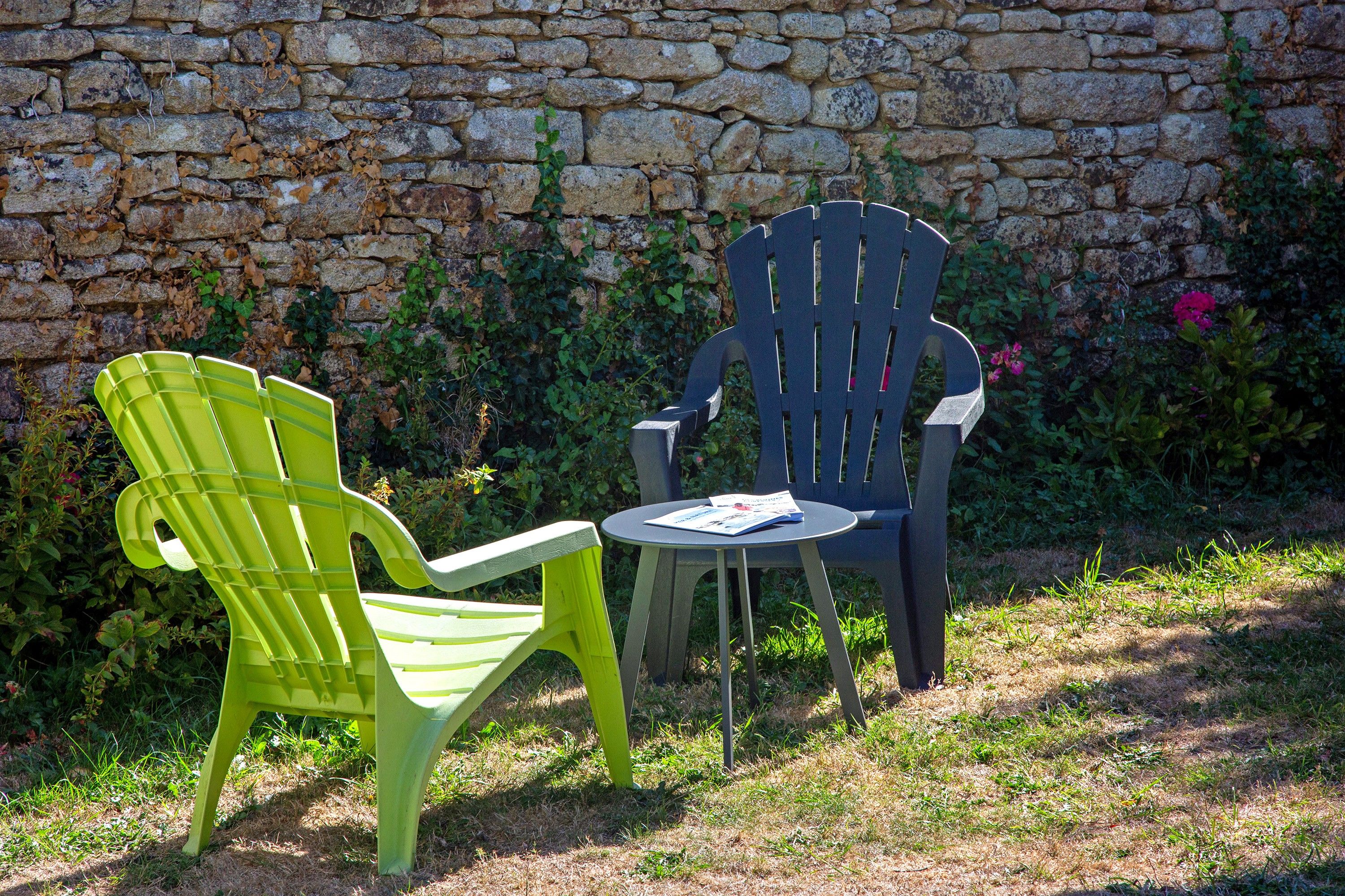 Two chairs and a small table set against a stone wall with greenery.