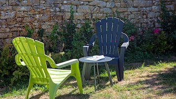 Two chairs and a small table set against a stone wall with greenery.