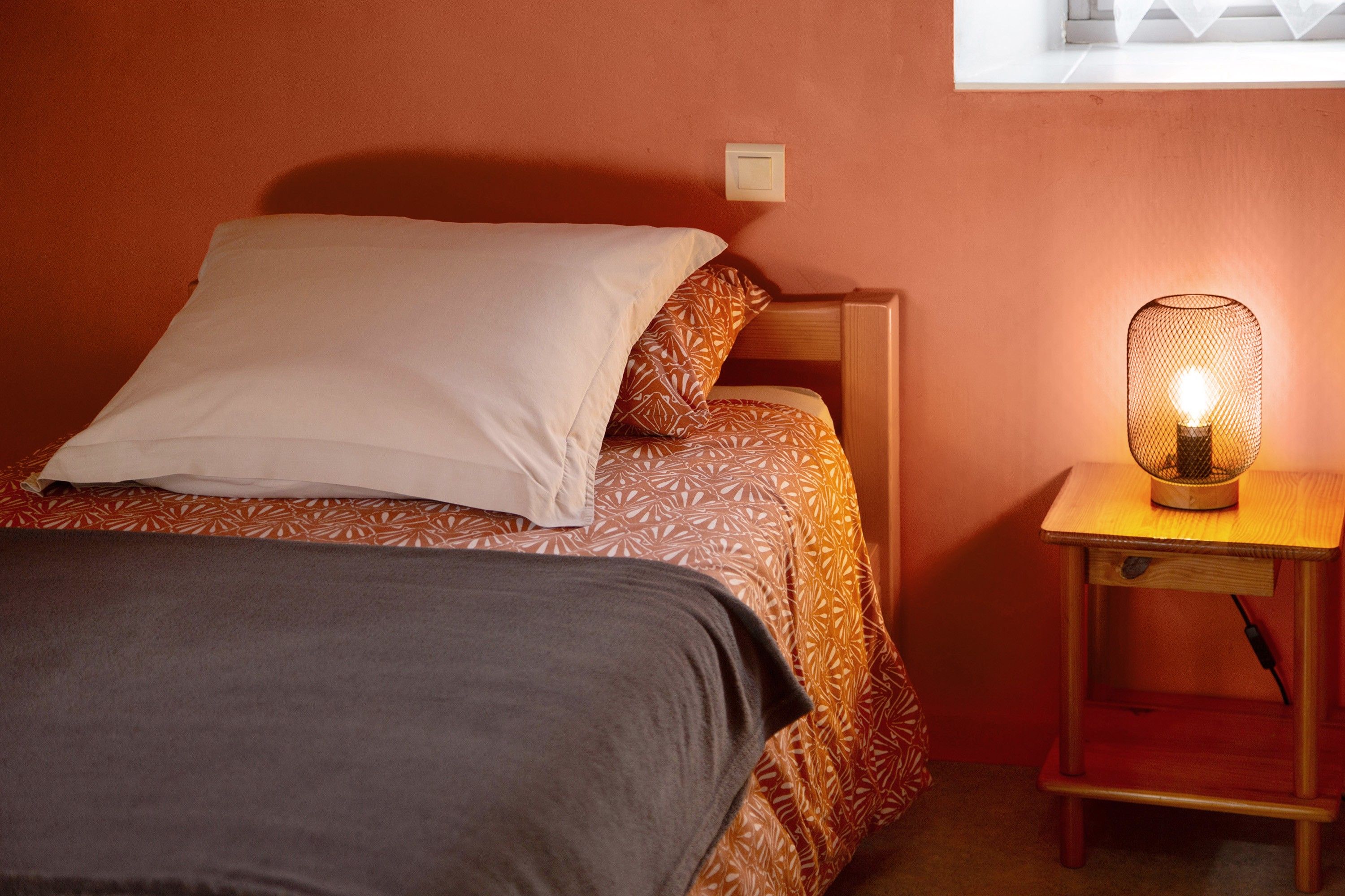 Un lit avec une literie à motifs, une table de chevet avec une lampe et un interrupteur mural.