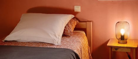 Un lit avec une literie à motifs, une table de chevet avec une lampe et un interrupteur mural.