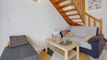 A cozy living area with a wooden staircase, a sofa, a small table with a vase of flowers, and a patterned pillow.