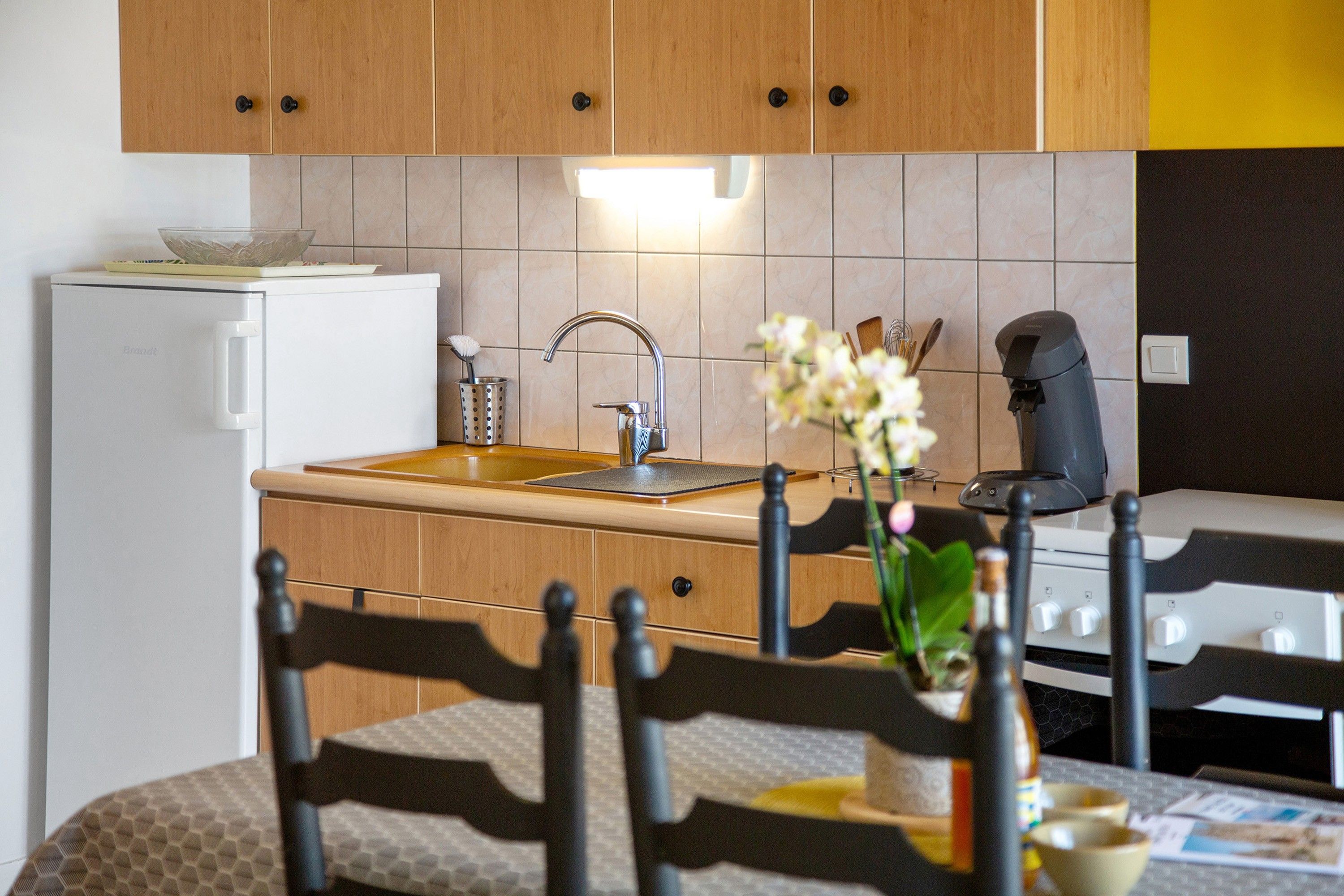 Une cuisine avec des meubles de rangement en bois, un réfrigérateur blanc, un évier en acier inoxydable et une machine à café.