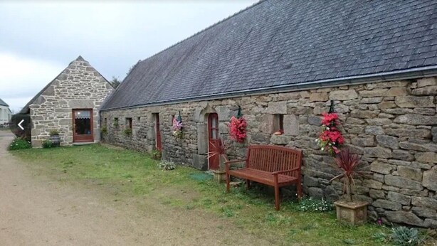 A stone building with a sloped roof, a bench, and potted plants.