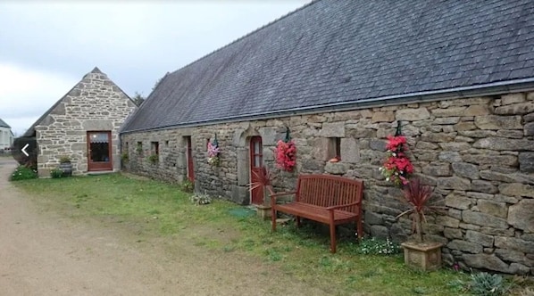 A stone building with a sloped roof, a bench, and potted plants.