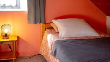 Una cama individual con una colcha estampada, una mesita de noche con lámpara y una ventana con cortinas.