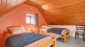 A cozy attic bedroom with two wooden beds, a small desk, and a chair.