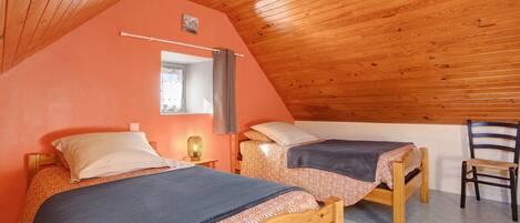 A cozy attic bedroom with two wooden beds, a small desk, and a chair.